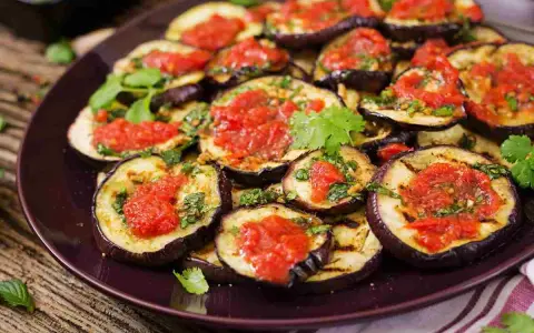 Fette di melanzane grigliate condite con salsa di pomodoro e basilico, un piatto gustoso di melanzane alla pizzaiola.