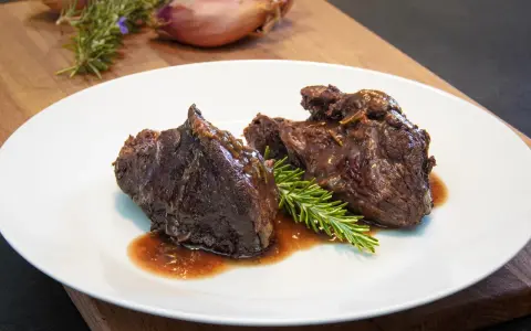Guancia di manzo brasata, tenera e succulenta, servita su un piatto bianco con rosmarino fresco. Un piatto che fa chiedere: guancia di manzo cos'è?