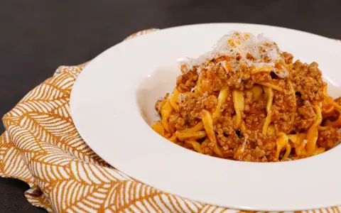 Tagliatelle ricche con sugo finto e parmigiano grattugiato, servite su un piatto bianco con tovagliolo decorato.