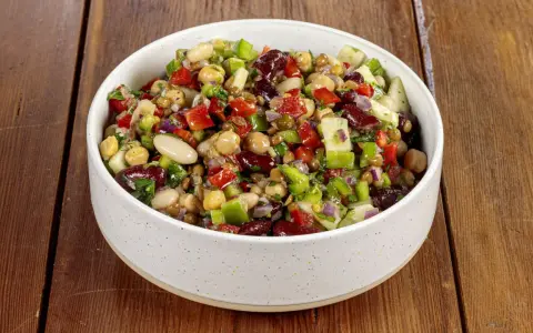 Una ciotola piena di colorata insalata di legumi, con ceci, fagioli, lenticchie, peperoni, cipolla rossa e prezzemolo fresco.