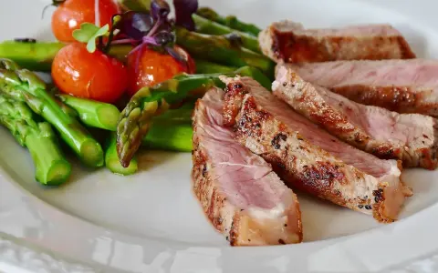 Fette di manzo magro cos'è? Succulenta carne con asparagi verdi e pomodorini su un piatto bianco.