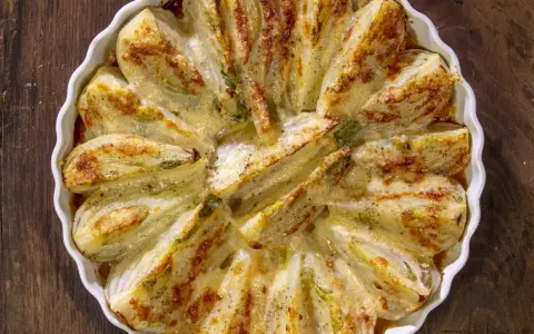 Finocchi al forno dorati e gratinati, serviti in una pirofila bianca su un tavolo di legno scuro.