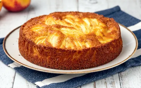 Torta di mele dorata, appena sfornata, con mele a vista. Perfetta da spennellare con un po' di sciroppo.