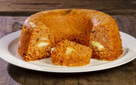 Un invitante timballo di riso, dorato e ripieno di formaggio filante, pronto per essere gustato su un piatto bianco.
