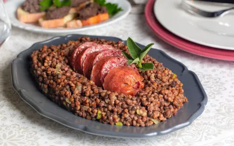 Piatto di lenticchie con fette di cotechino, un classico su come si fa il cotechino. Guarnito con salvia.