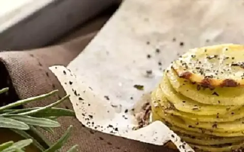 Deliziosa torretta di patate, sottili fette impilate e condite con erbe aromatiche e pepe nero, su carta da forno.