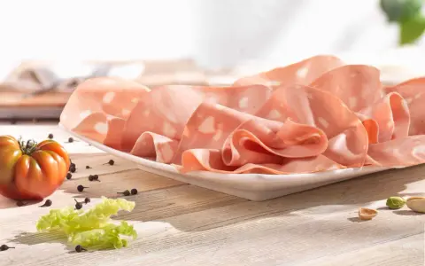 Fette di mortadella su piatto bianco, con pomodoro, lattuga e pepe. La differenza tra mortadella e bologna è nella qualità e negli ingredienti.