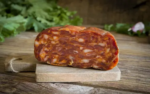 Un pezzo di salame stagionato su tagliere di legno. La differenza tra salame e sopressa è nella grana: qui si vede la carne tritata grossolanamente.
