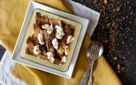 Carciofi e ricotta al forno in una teglia bianca, guarniti con pangrattato croccante. Serviti su un tovagliolo giallo.