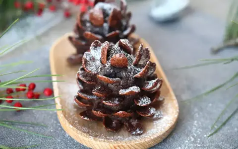 Deliziose pigne dolci decorate con zucchero a velo, su un vassoio di legno, con rami di pino e bacche rosse sullo sfondo.