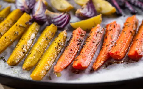 Carote, cipolle rosse e patate dorate, un tripudio di verdure al forno, condite con erbe aromatiche e olio.