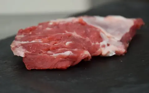 Un succulento spider steak crudo, con venature di grasso bianco, pronto per essere cucinato su una pietra scura.