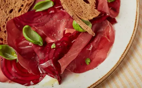 Fette di bresaola e barbabietola, esempi di salumi non insaccati quali sono, con crostini e basilico.