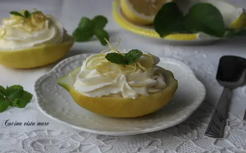 Deliziosa mousse al limone servita in un limone svuotato, guarnita con scorzette e menta.