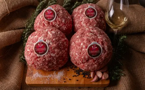 Quattro sfere di carne macinata TASTASAL, con rosmarino, aglio, pepe e sale su un tagliere. Ingredienti freschi per un sapore autentico.