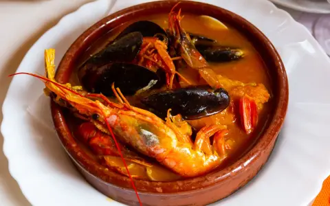 Una ricca zuppa di pesce in ciotola di terracotta, con gamberoni, cozze e pomodorini.