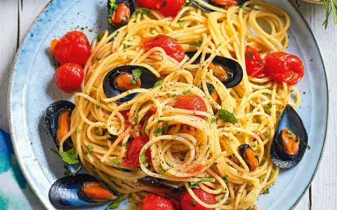 Un piatto invitante di spaghetti con le cozze e pomodorini, condito con prezzemolo fresco e pepe nero.