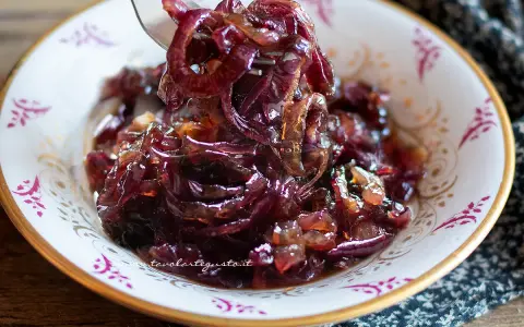 Un cucchiaio solleva un mucchietto di cipolle caramellate, lucide e invitanti, in una ciotola decorata.