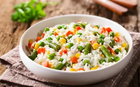 Un piatto di riso per insalata di riso, con piselli, carote, fagiolini e mais, su un tovagliolo di stoffa marrone.
