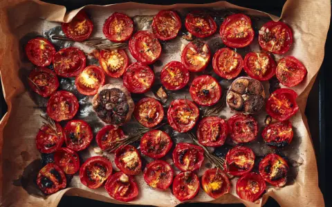 Pomodori al forno, caramellati e succosi, con aglio arrostito e rosmarino su carta forno.