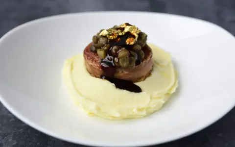 Piatto moderno con lenticchie e cotechino, un omaggio alla tradizione, servito su purè di patate e decorato con oro edule.