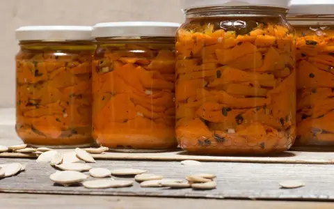 Barattoli di zucca sott'olio in agrodolce, con semi di zucca sparsi sul tavolo di legno.
