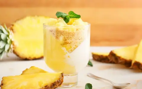 Delizioso dolce con ananas fresco, yogurt e crumble. Un bicchiere pieno di gusto tropicale, con fette di ananas e menta a guarnire.