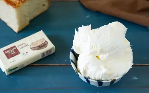 Burro montato in una ciotola, pronto per essere spalmato sul pane. La confezione di burro salato è accanto.