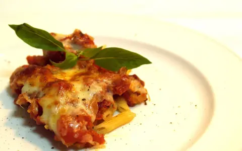 Porzione di pasta ncasciata fumante, con formaggio filante e basilico fresco, su un piatto bianco.