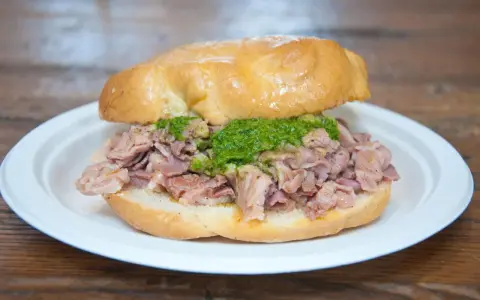 Panino con lampredotto, un classico street food fiorentino. La ricetta prevede trippa di bovino cotta e servita in un panino morbido con salsa verde.