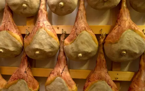 Filetti di salumi appesi a stagionare su scaffali di legno.