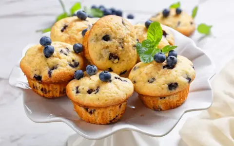 Muffin ai mirtilli appena sfornati, decorati con mirtilli freschi e menta. Una deliziosa ricetta per iniziare la giornata.