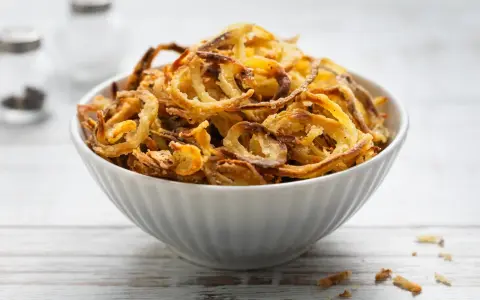 Ciotola piena di croccanti cipolle fritte dorate, perfette per accompagnare ogni piatto.