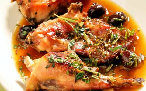 Coniglio alla ligure succulento, con olive nere e erbe aromatiche, immerso in un sugo dorato.