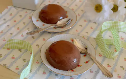Due budini al cioccolato con amido di mais, serviti su piattini floreali con cucchiaini d'argento. Nastro a quadretti verdi completa la scena.