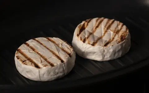 Due forme di formaggio da fare alla piastra, con belle striature dorate, cuociono in una padella scura.