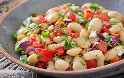 Insalata di fagioli bianchi, pomodori freschi, cipolla rossa e erbe aromatiche in una ciotola rustica. Un piatto colorato e salutare.