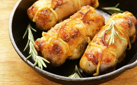 Involtini di pollo al forno dorati e succulenti, legati con spago da cucina e guarniti con rametti di rosmarino fresco, serviti in una padella di ghisa.