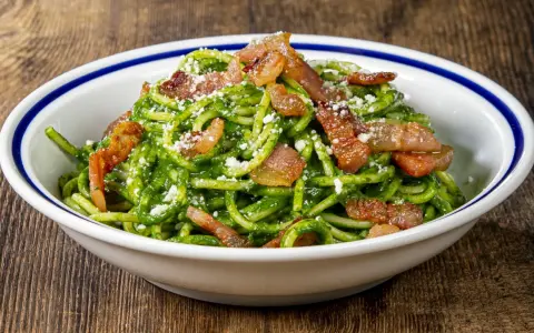 Un piatto invitante di pasta con spinaci, condita con croccante pancetta e parmigiano grattugiato, servita in una ciotola bianca con bordo blu.