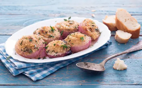 Deliziose cipolle al forno, dorate e profumate, servite su un piatto bianco con pane croccante e un cucchiaio d'argento.