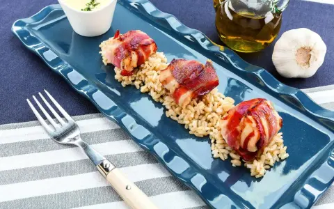 Tre bocconcini di pollo con pancetta avvolti e dorati, serviti su un letto di riso integrale.