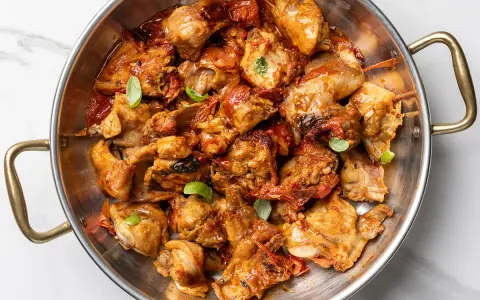 Un saporito coniglio all'ischitana, cotto in padella con pomodoro e basilico, pronto per essere gustato.