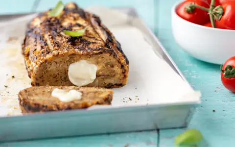 Polpettone di melanzane grigliato, ripieno di formaggio filante, su teglia con basilico e pomodorini.