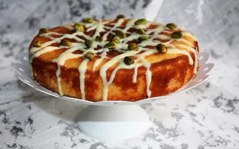 Deliziosa torta al bergamotto, decorata con glassa bianca e pistacchi croccanti, pronta per essere gustata.