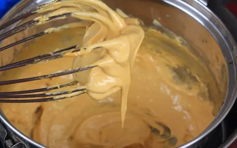 Una frusta raccoglie una crema densa e dorata, pronta per diventare uno zabaione freddo.