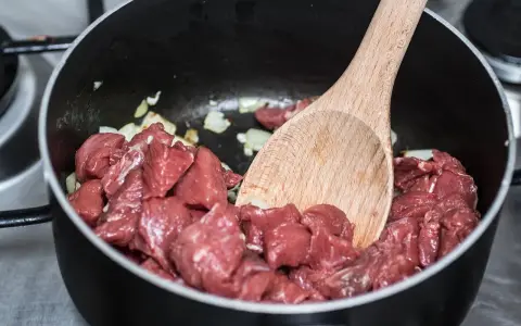 Bocconcini di manzo crudo in padella con cipolla, pronti per diventare uno spezzatino gommosa di manzo.