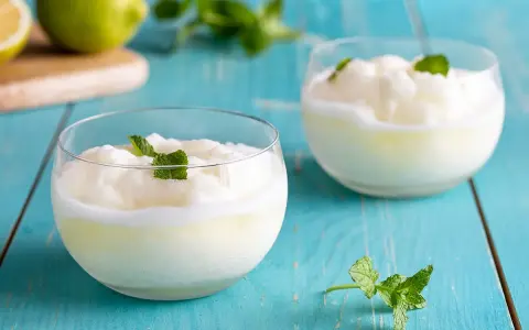 Sorbetto al limone senza gelatiera: due coppette di fresco sorbetto al limone guarnite con menta, su un tavolo di legno blu.