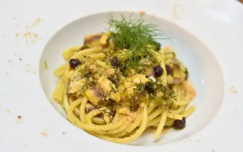 Un piatto invitante di pasta con finocchi, olive e acciughe, guarnito con erbe fresche e pangrattato.