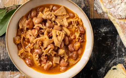 Piatto fumante di trippa alla milanese con fagioli, su un tavolo di legno rustico, accanto a pane casereccio.