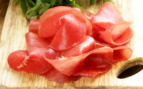 Fettine sottili di salume simile alla bresaola, rosse e lucide, disposte su un tagliere di legno con un ciuffo di prezzemolo.